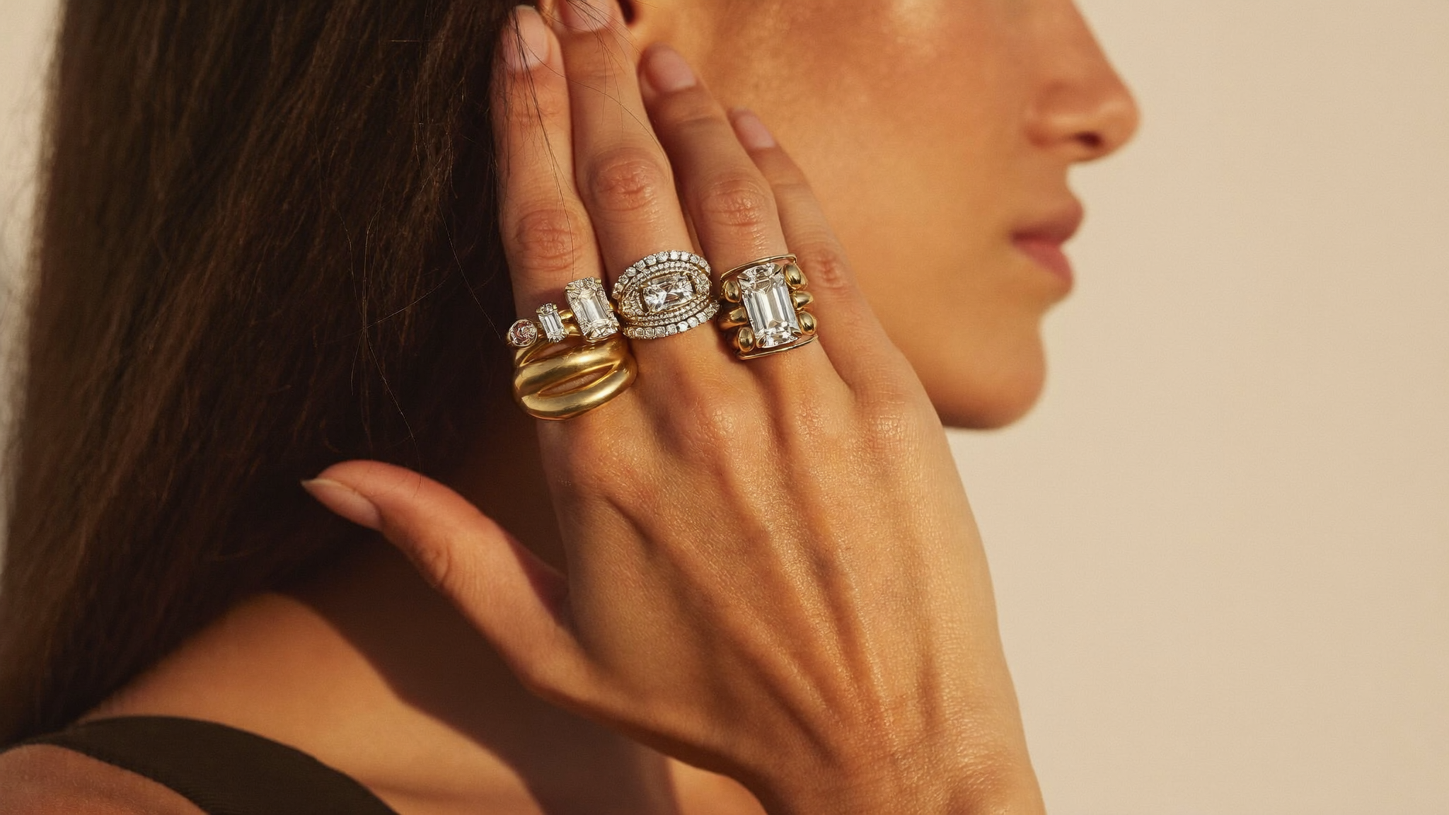 A hand wearing bold sculptural yellow-gold lab-grown diamond statement rings stacked together in warm golden light