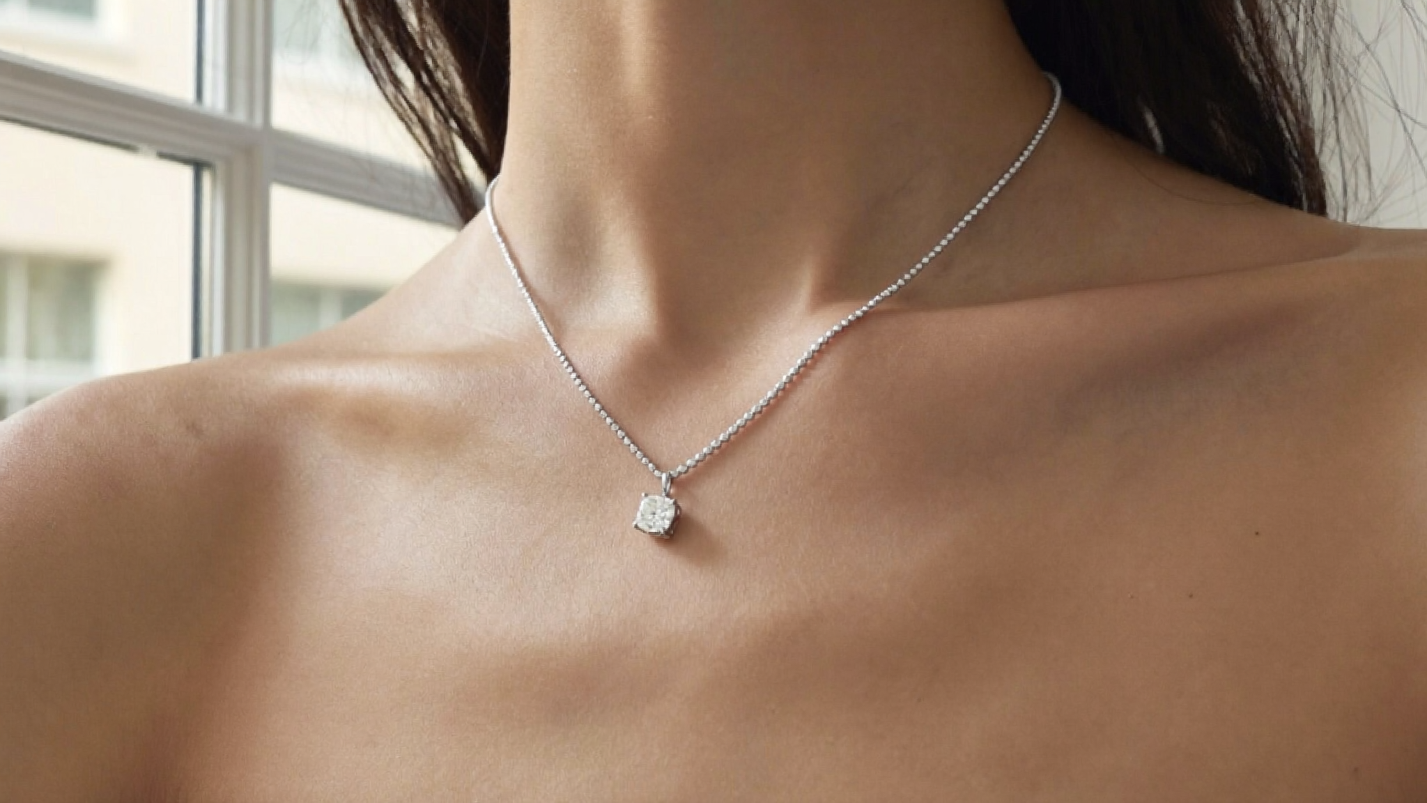 A delicate lab-grown diamond solitaire pendant resting on a collarbone in soft natural light