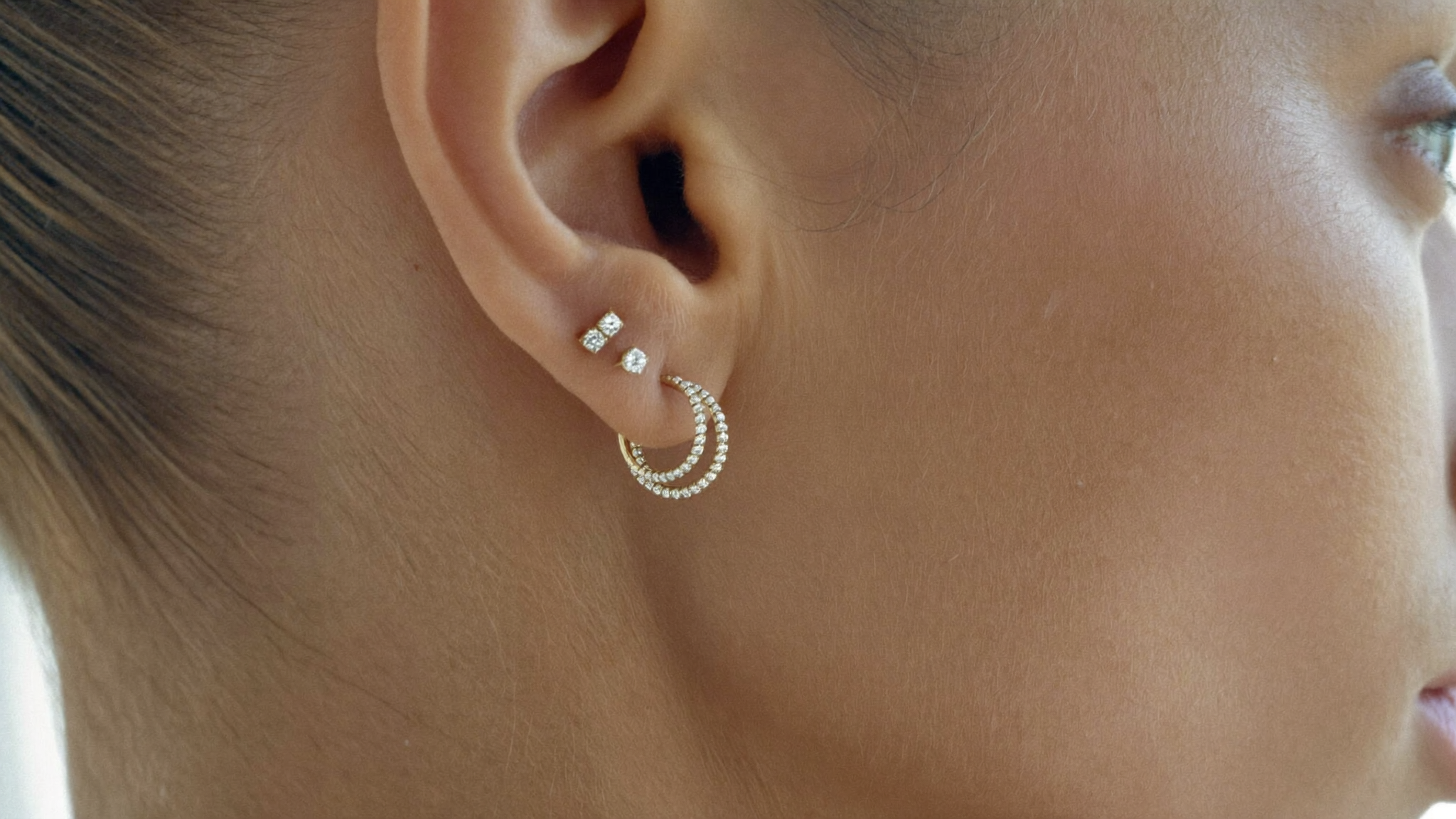 Close-up of a curated ear stack with gold diamond hoops, a huggie, and a stud, warm natural light