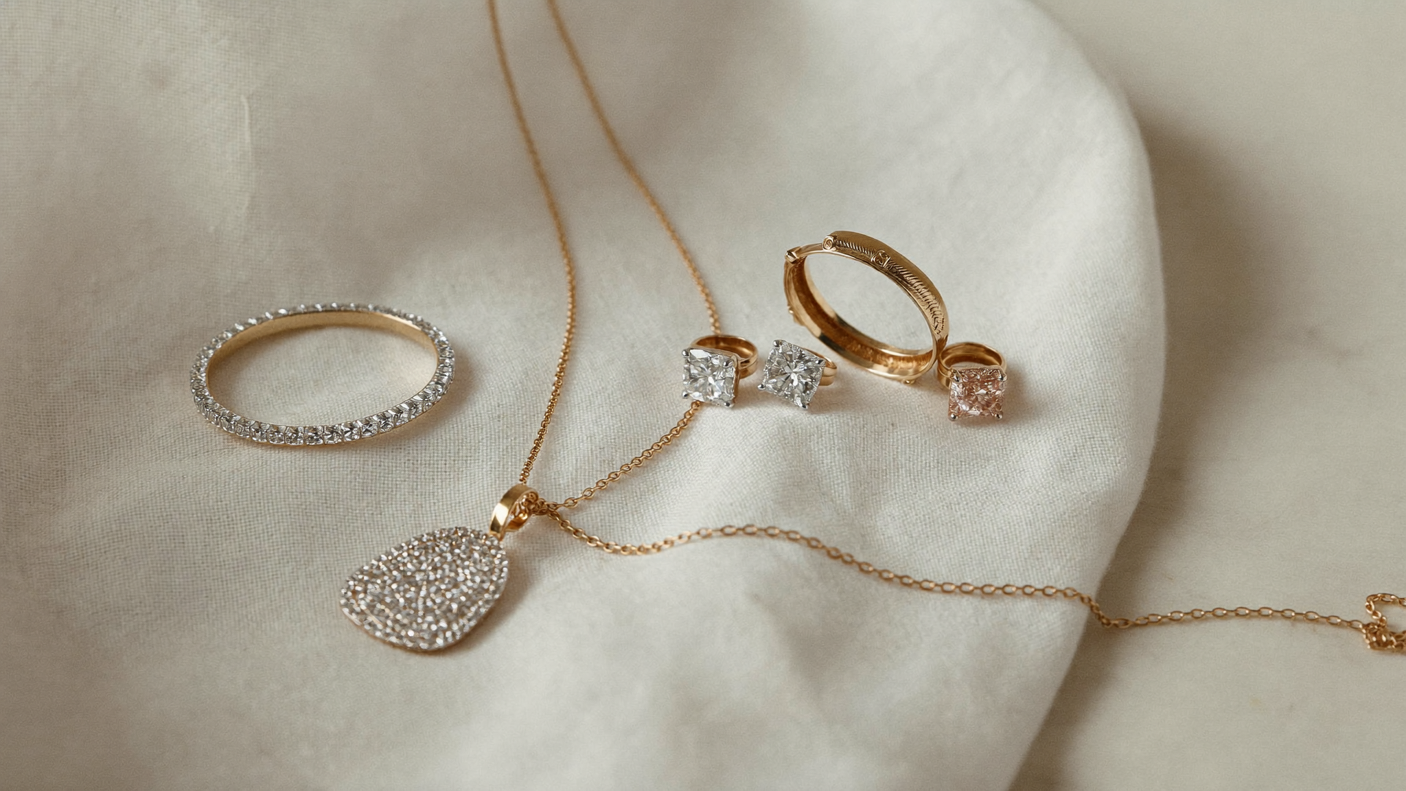 Yellow gold, white gold and rose gold diamond jewelry flat-lay on ivory linen in soft natural light
