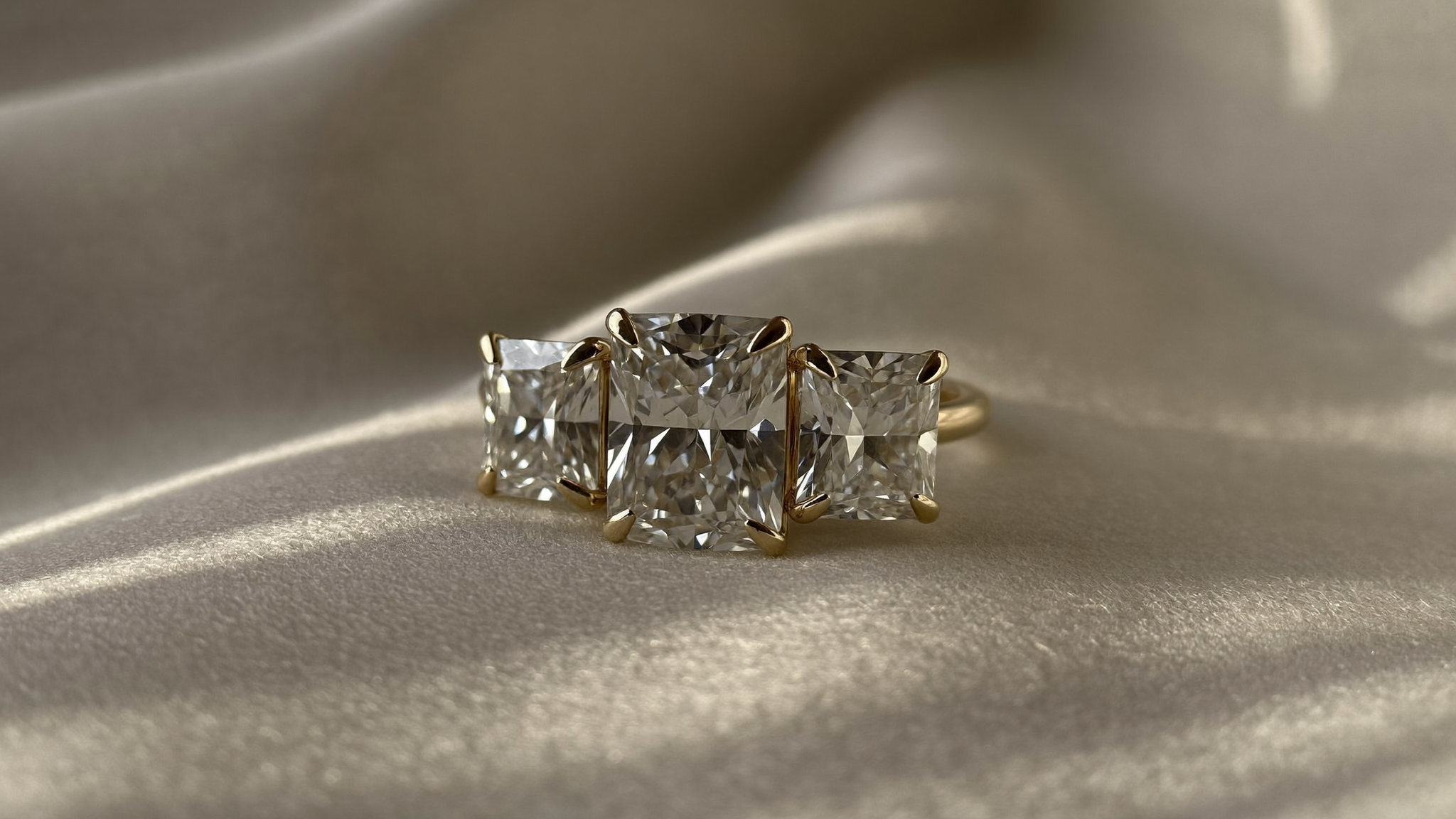 Close-up of a three-stone lab-grown diamond ring in gold on ivory linen, natural light