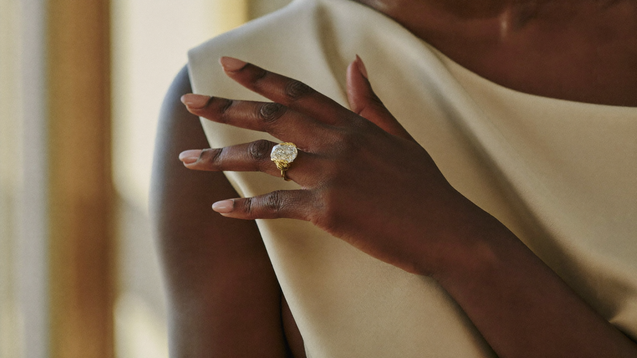 Right-hand ring: a woman's right hand wearing a bold sculptural lab-grown diamond ring in solid gold on cream silk in natural light