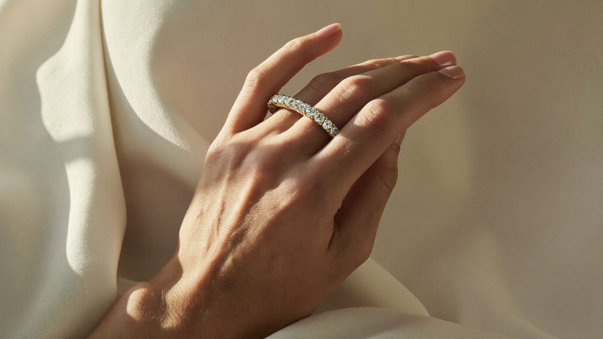 Close-up of a diamond eternity band in yellow gold on ivory linen in natural light