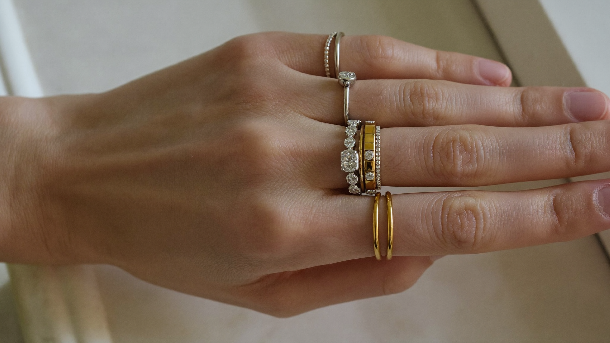 Stacked diamond rings and slim gold bands layered across a hand in natural light