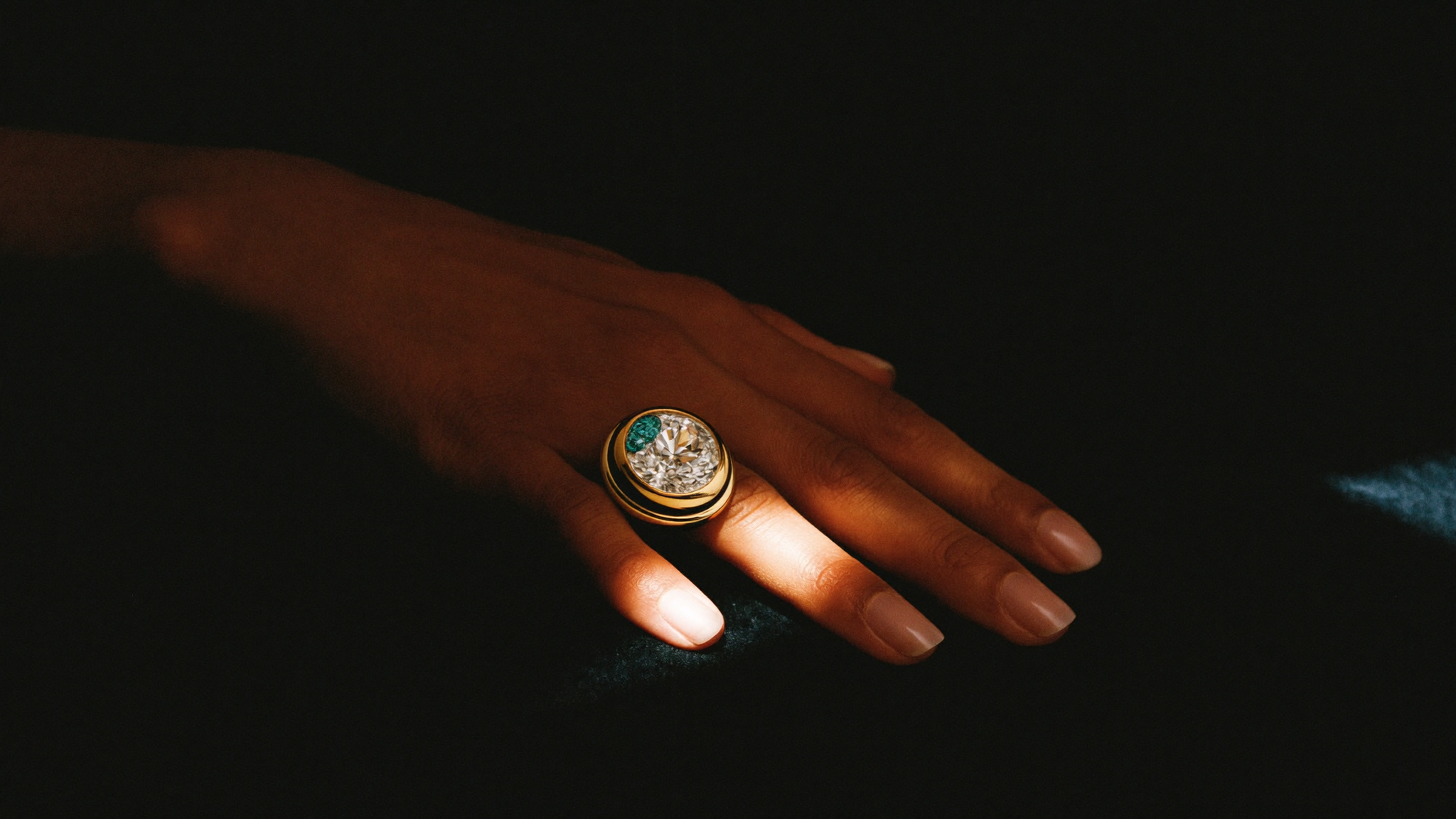 Bold sculptural gold cocktail ring with a large diamond and aquamarine on a hand, editorial lighting