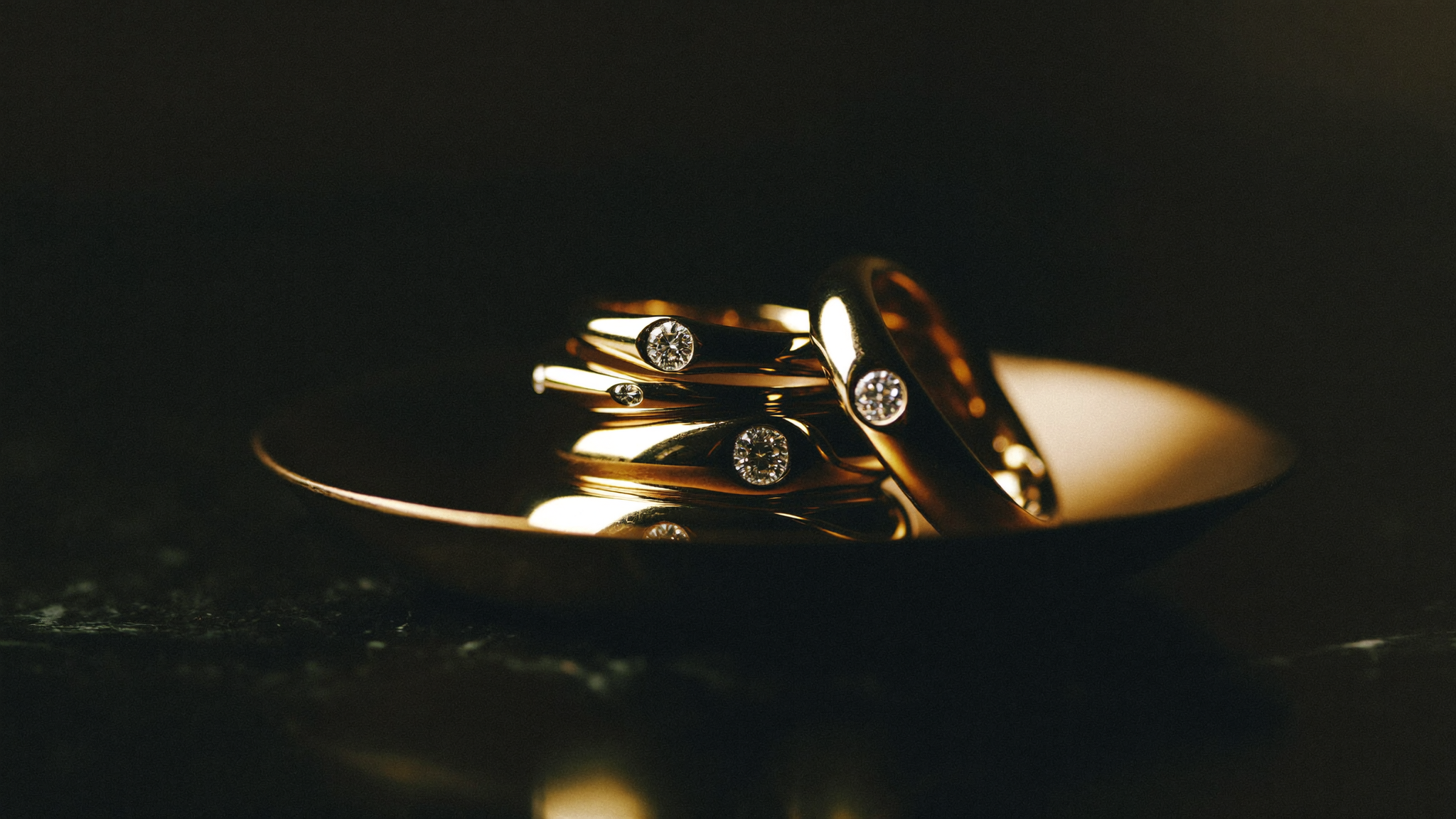 Solid gold diamond rings and bands stacked in a brass dish in warm light, showing solid gold jewelry