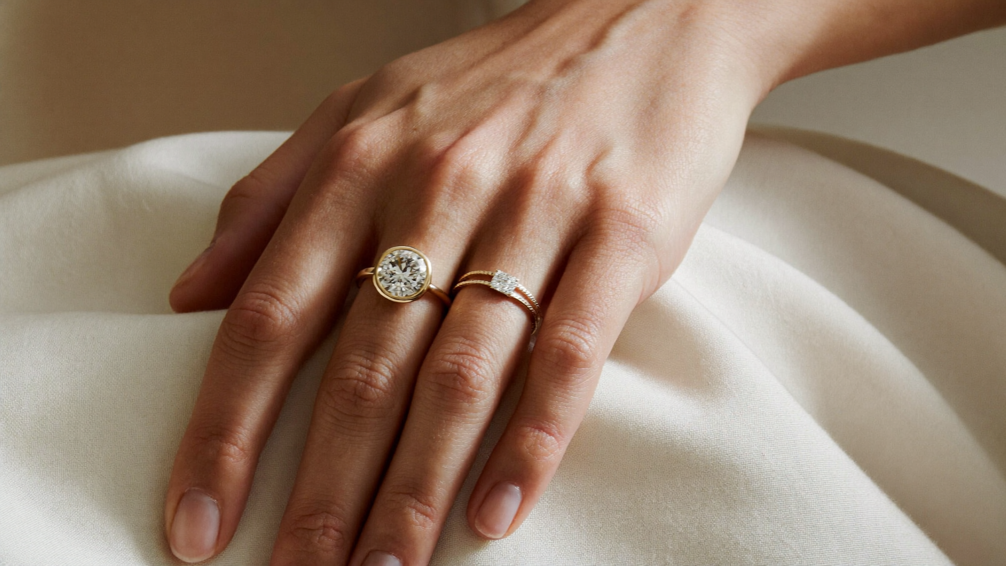 Close-up of solid gold lab-grown diamond engagement ring settings, bezel, pave and channel, on ivory linen in natural light