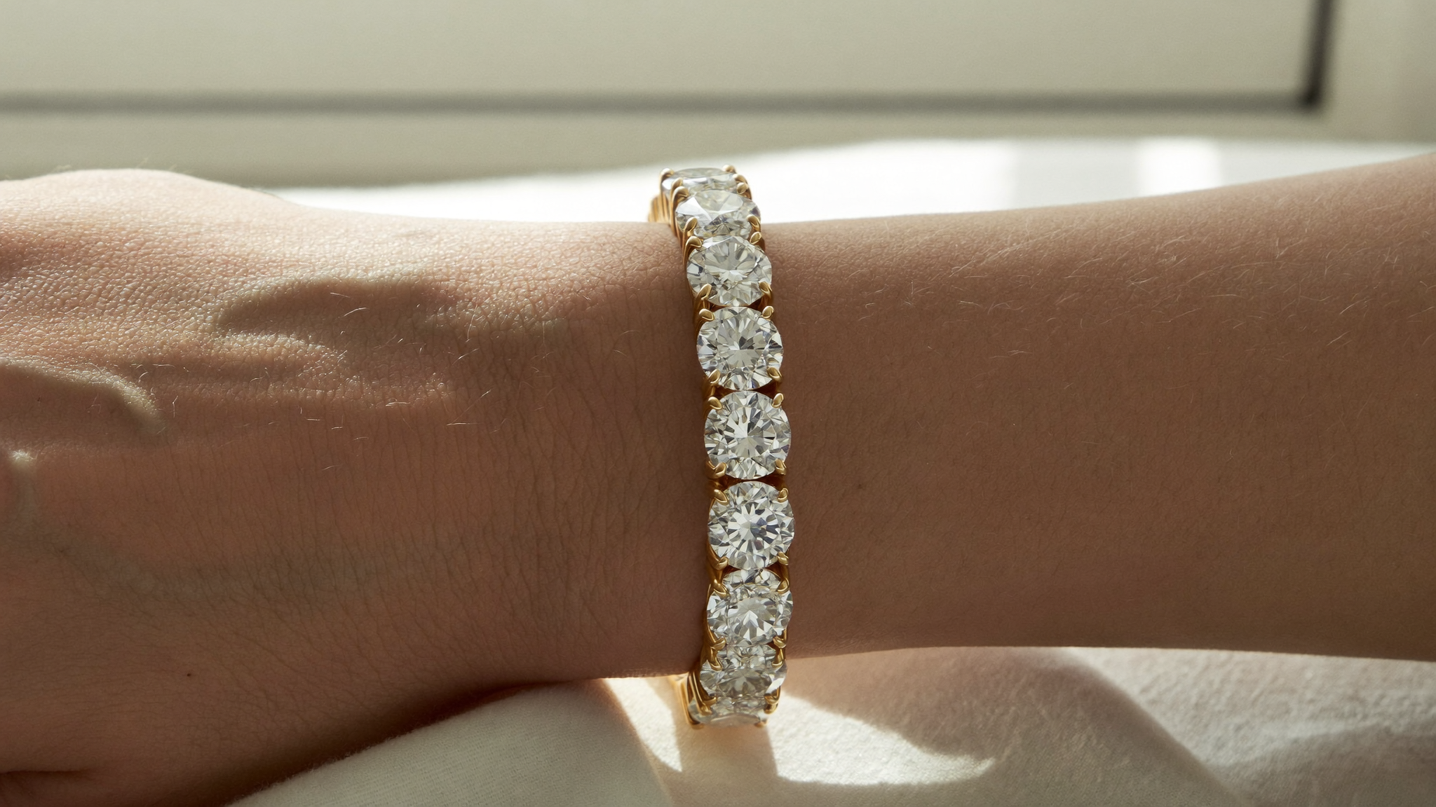 Lab-grown diamond tennis bracelet in solid gold on a woman's wrist on linen, natural light