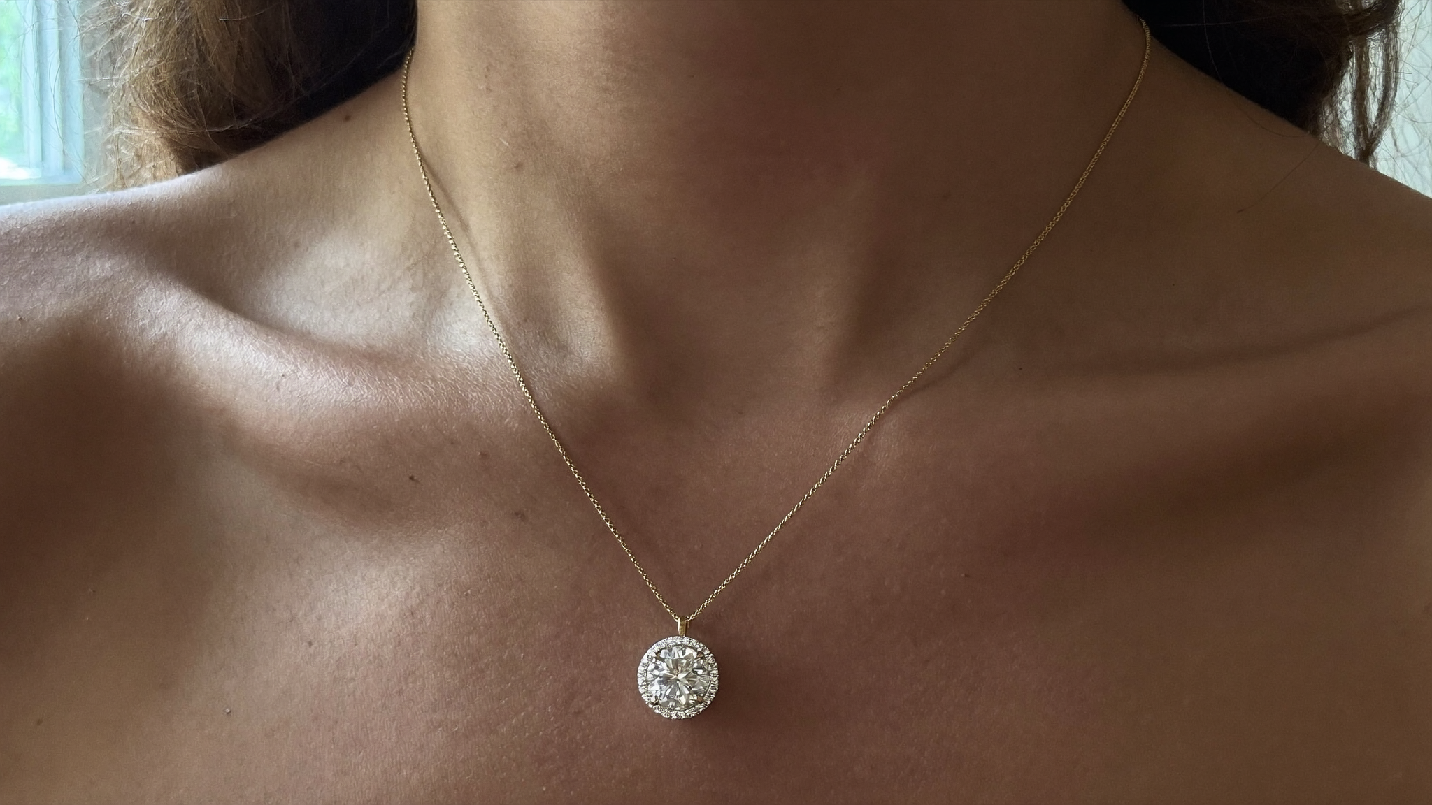Diamond solitaire necklace with a single bezel-set stone on a fine gold chain at the collarbone, natural light