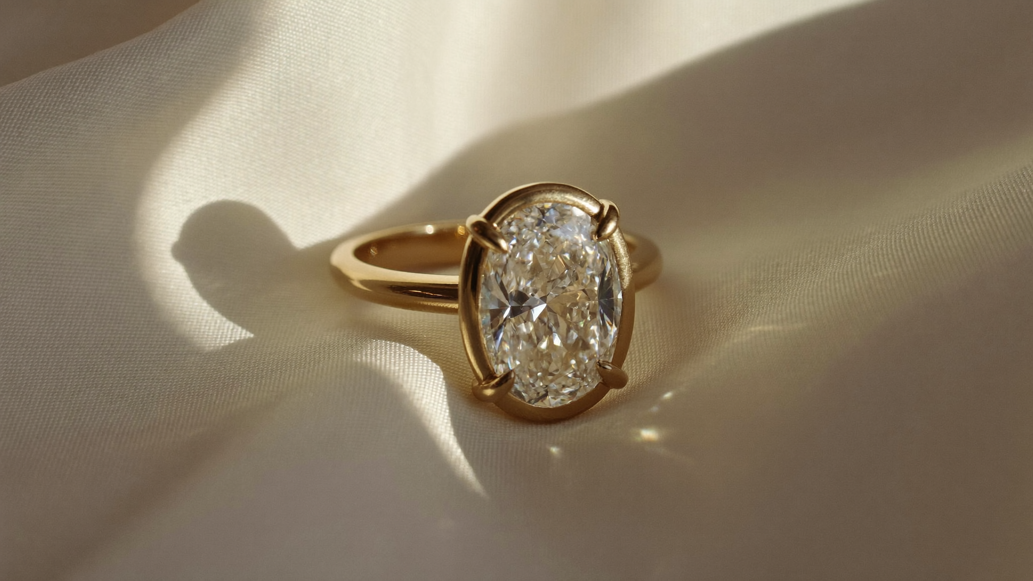 Oval cut diamond solitaire ring in solid gold resting on ivory silk in natural light