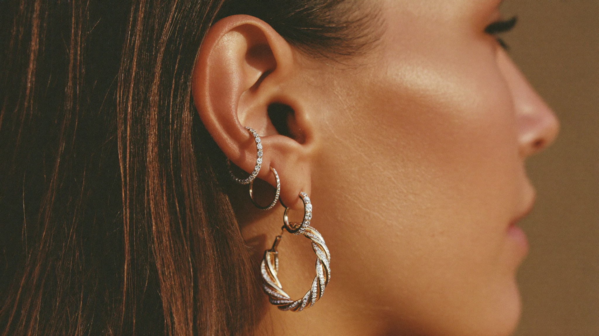 Stacked diamond hoop earrings in solid gold on a model's ear in warm golden light