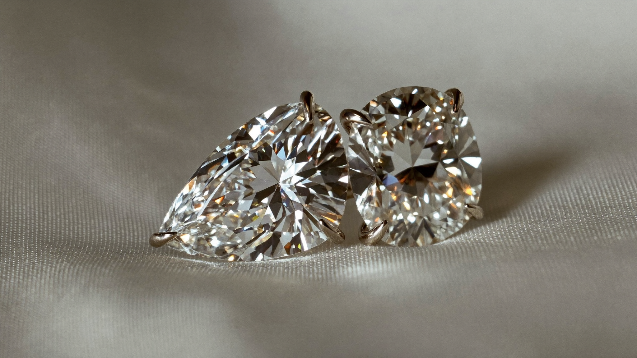 Two lab-grown diamonds set side by side representing a toi et moi ring, on ivory silk in natural light