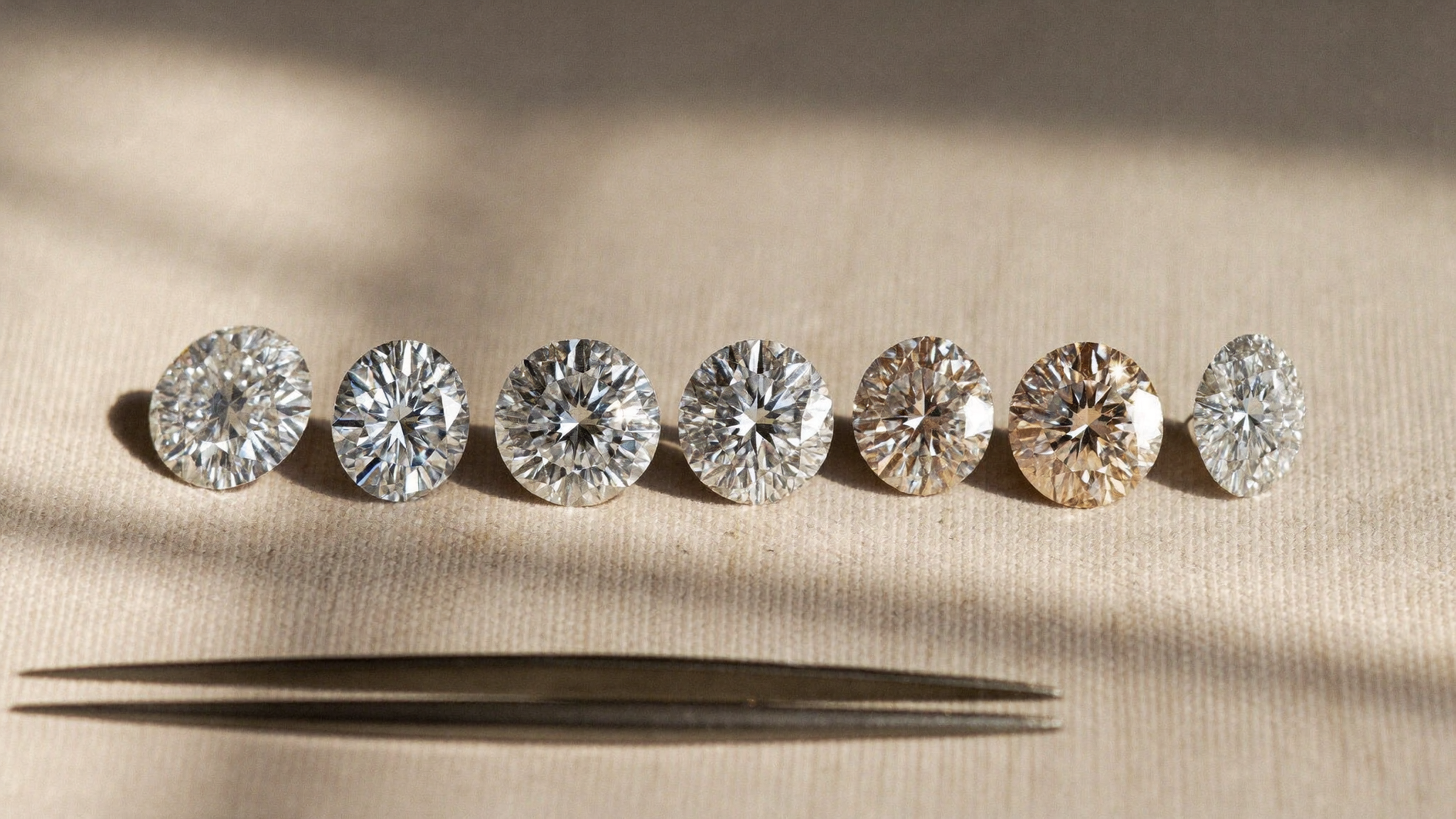 Row of lab-grown diamonds along the diamond color chart, from icy colorless to warm champagne, on linen in natural light