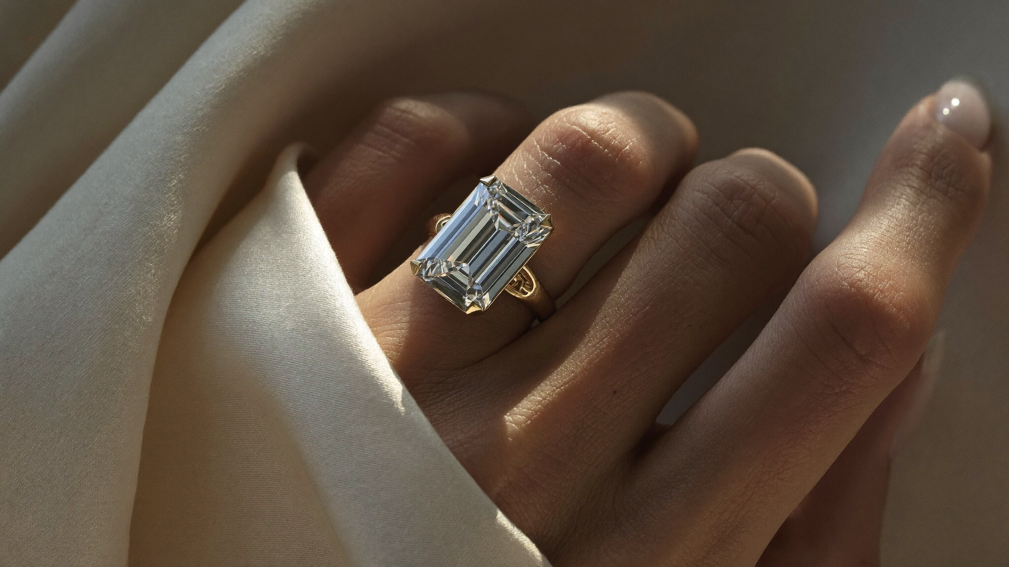 Emerald cut engagement ring in solid gold on a woman's hand over ivory silk in warm natural light