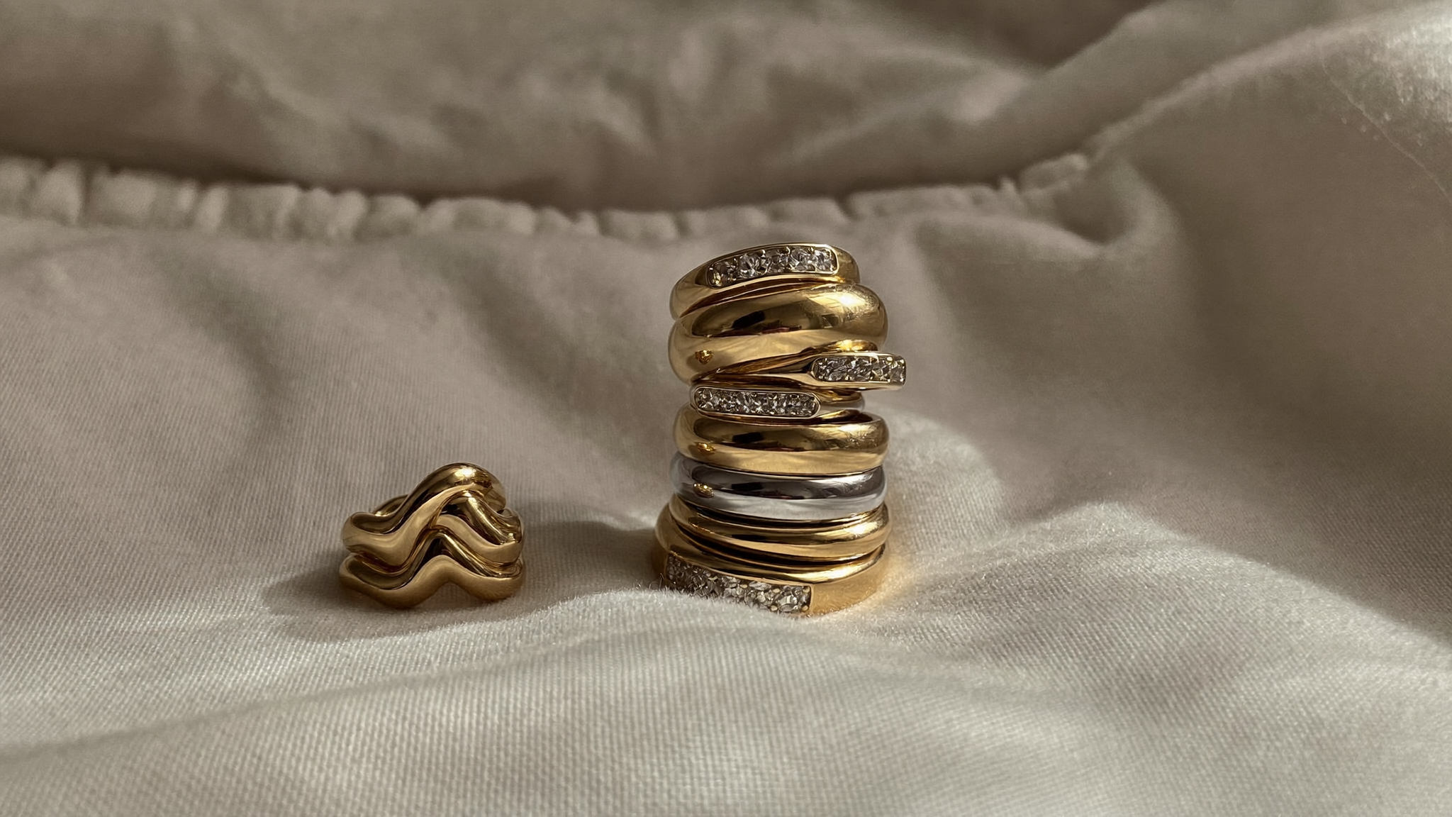 Stack of solid gold diamond band rings in 10k, 14k and 18k gold on cream linen, natural light