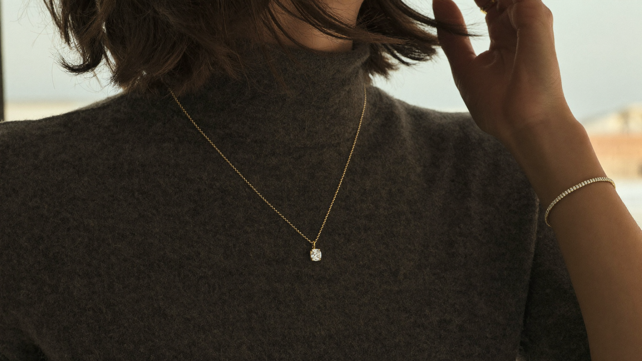 Winter jewelry trends 2026 shown as a solid gold diamond pendant and diamond line bracelet worn over charcoal cashmere