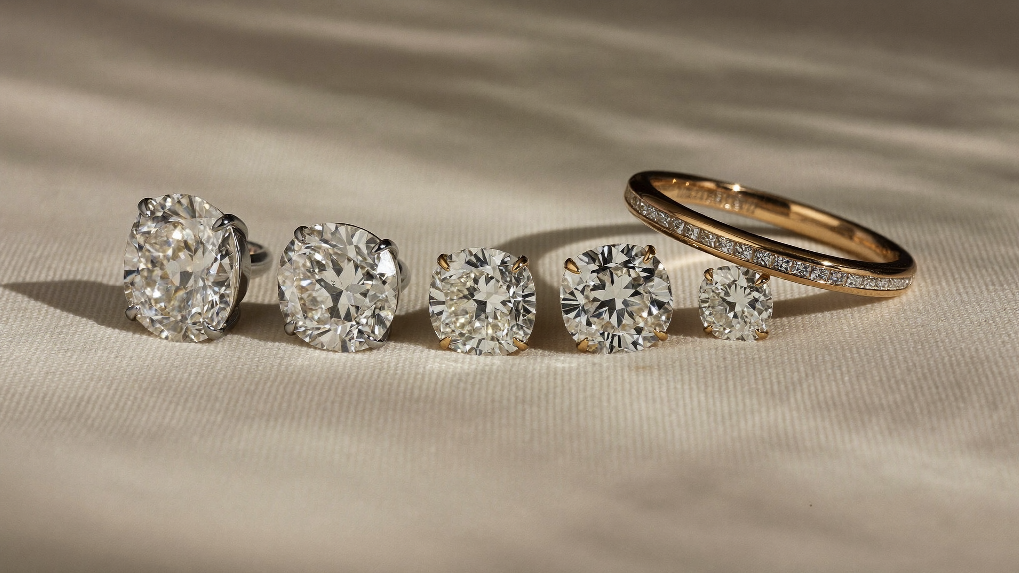 Loose lab grown diamonds in graduated carat sizes on cream linen beside a solid gold eternity band, illustrating why lab grown diamond prices fell in 2026