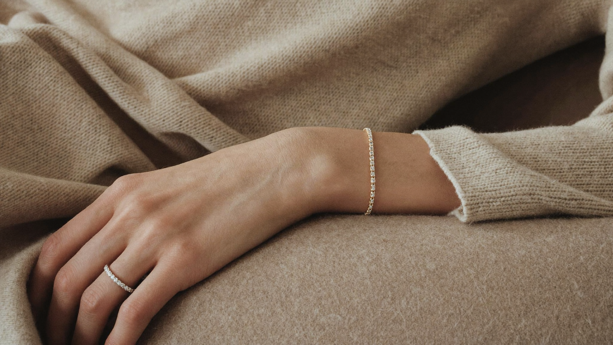 Quiet luxury jewelry styled on cashmere: a slim solid gold diamond tennis bracelet and a narrow pave diamond band