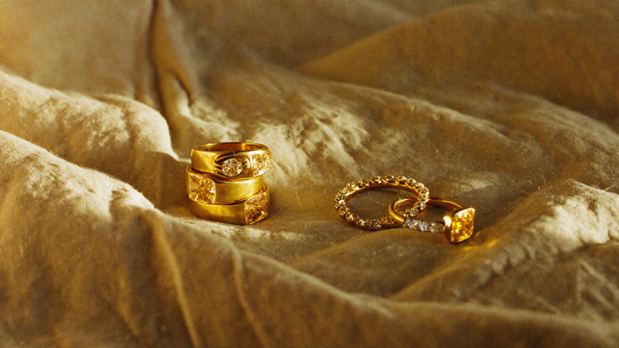 Yellow gold jewelry trend 2026: a stack of warm yellow gold diamond rings and a gold diamond hoop on oatmeal linen in low sun