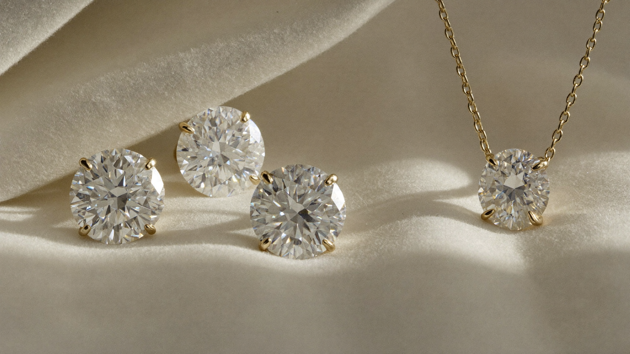 Near-colorless lab-grown diamonds on ivory linen beside a gold solitaire pendant, a close look at diamond color grade