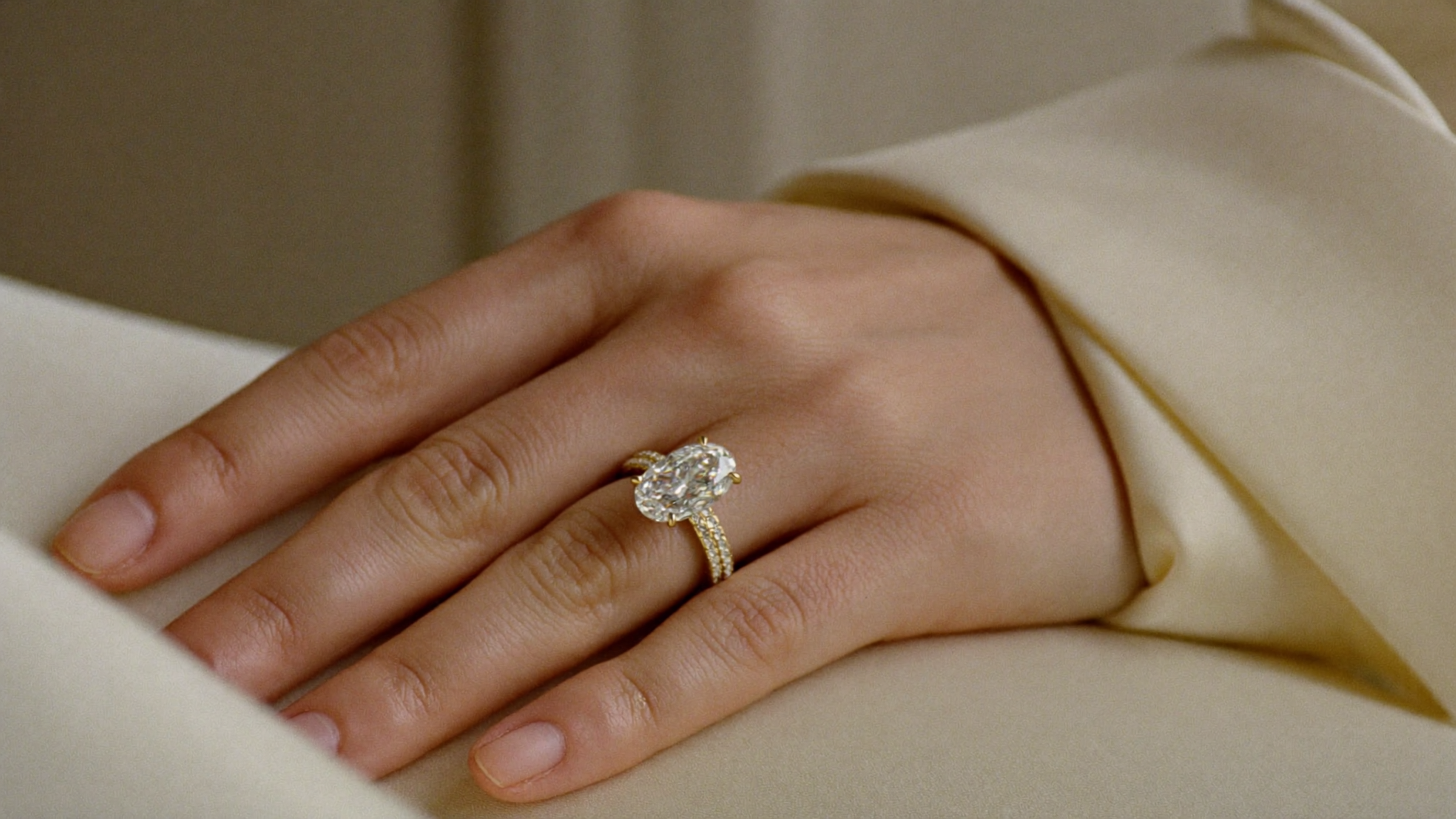Engagement ring trends 2026: a yellow gold oval diamond engagement ring on a hand resting on cream silk