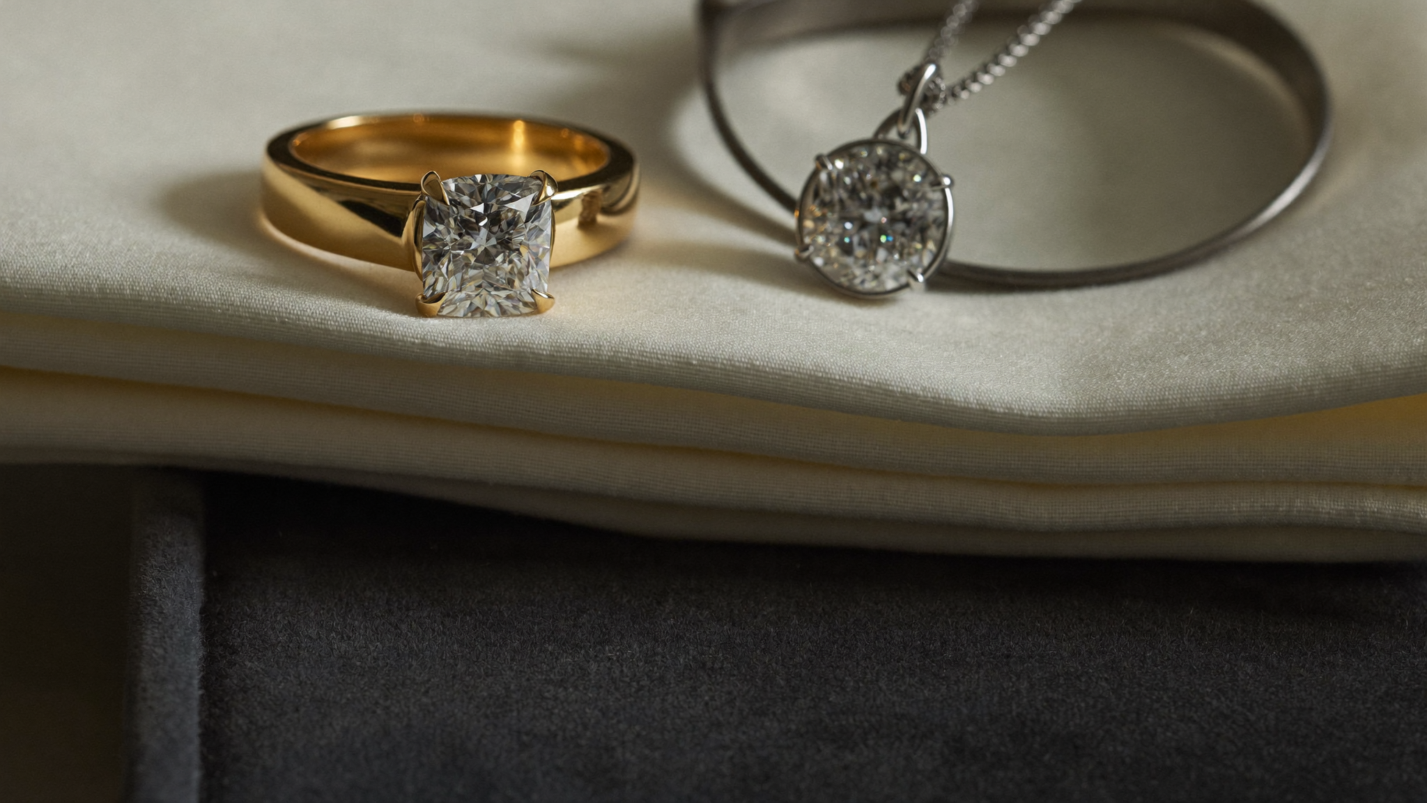 Gold lab-grown diamond ring and diamond pendant on ivory linen, a reference image for how to insure a diamond ring