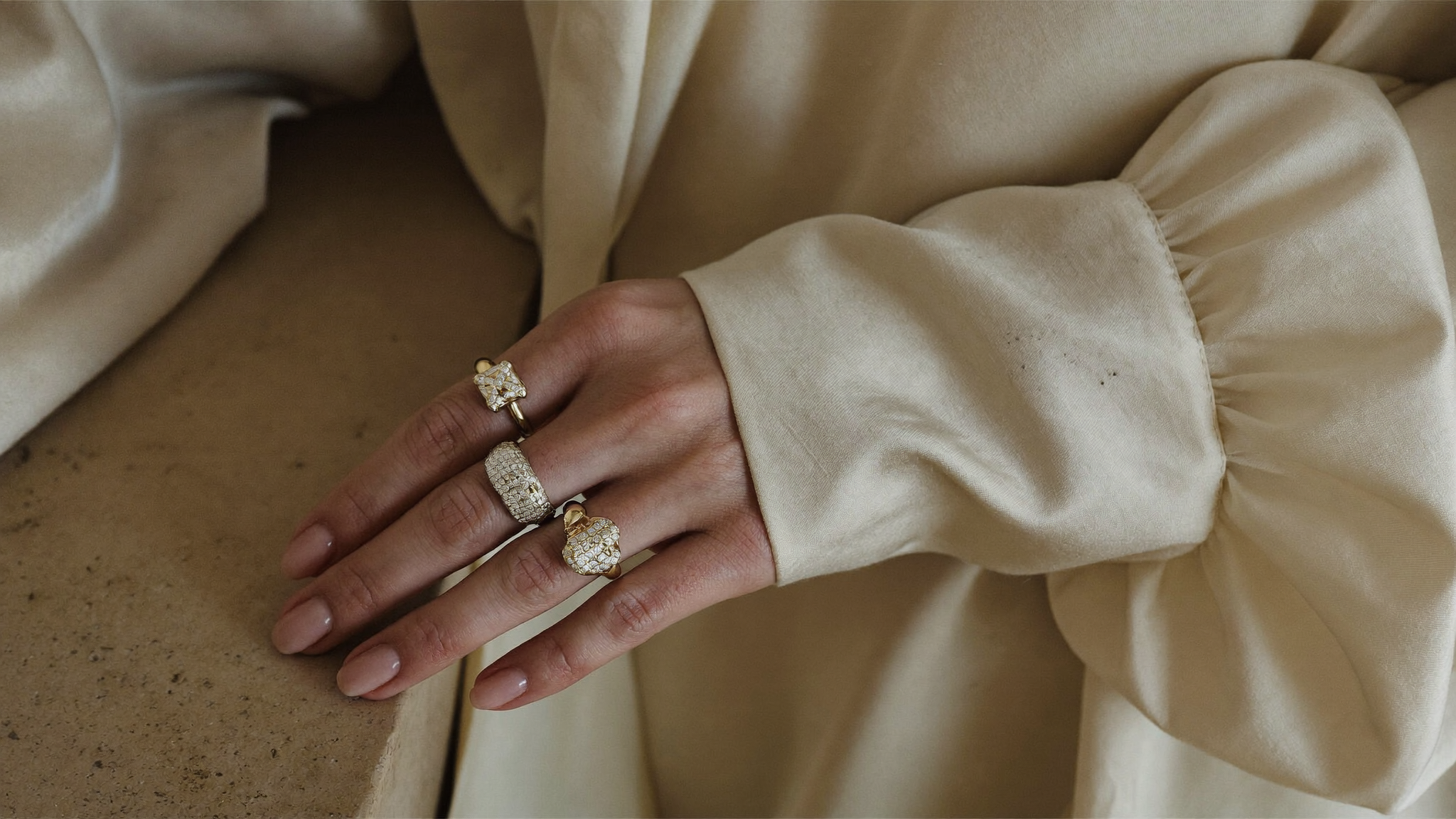 Woman's right hand wearing three sculptural gold lab-grown diamond right hand rings against cream silk