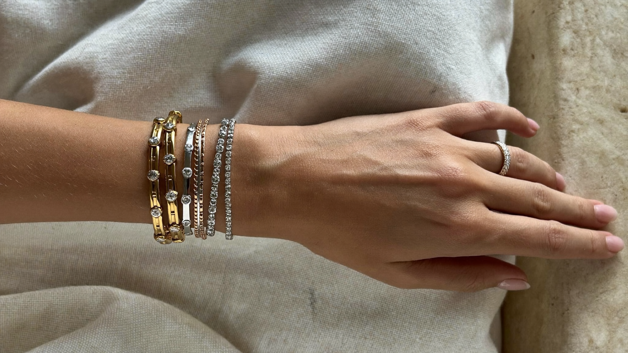 Yellow gold and white gold diamond tennis bracelets layered on a wrist with a rose gold ring, mixing metals jewelry styling