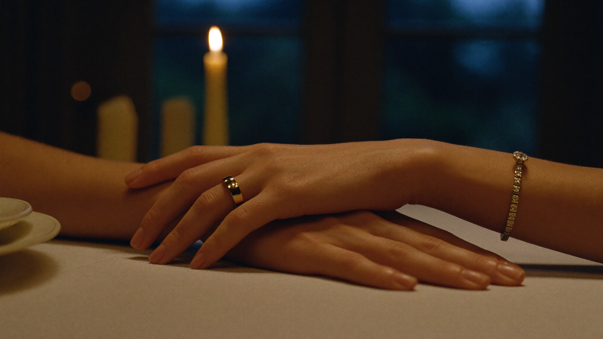 Hands at a candlelit table wearing a gold diamond eternity band and tennis bracelet, anniversary jewelry gifts