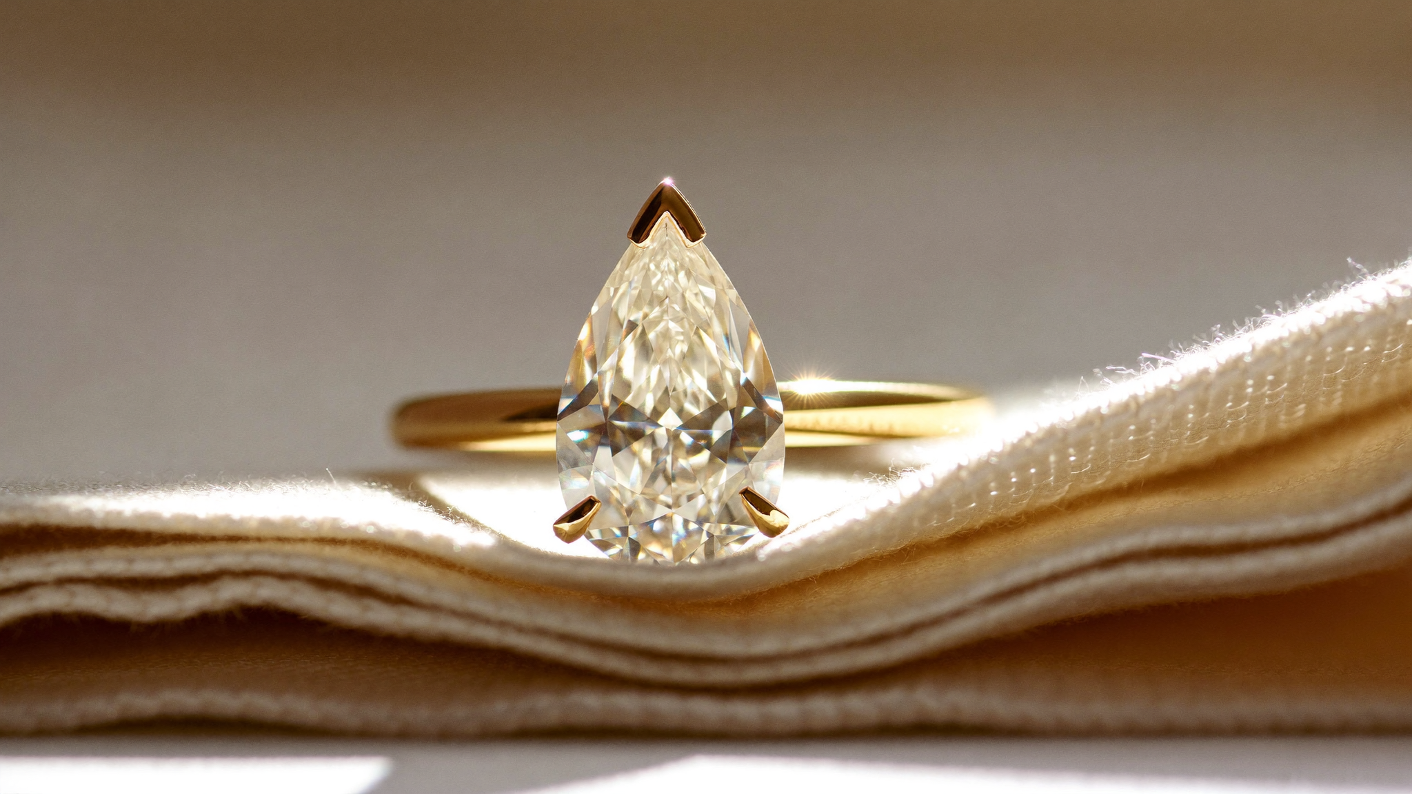 Pear shaped diamond ring in solid yellow gold on linen, close-up in natural light