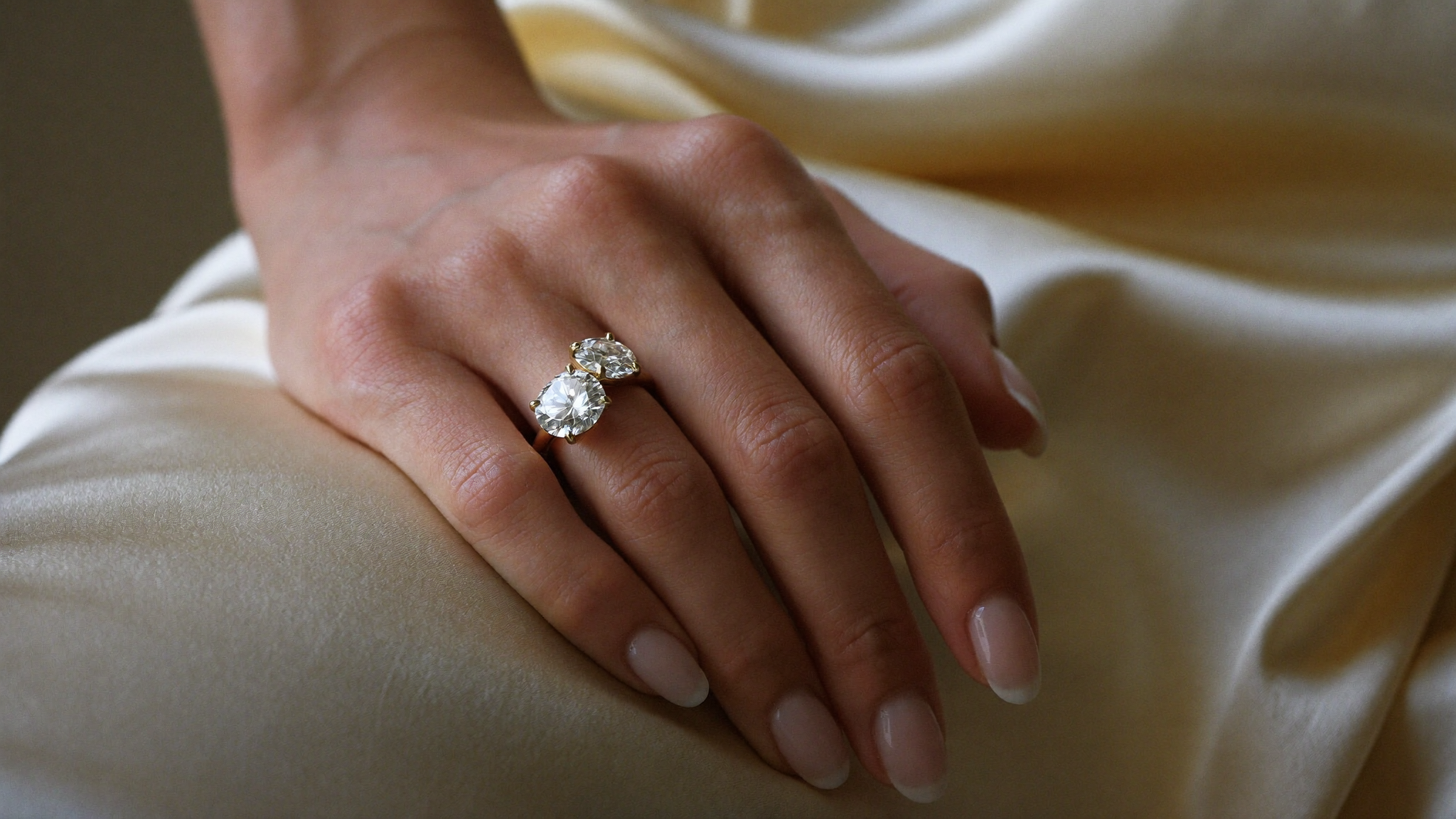 Toi et moi rings: two-stone diamond ring in solid yellow gold on a hand, soft natural light