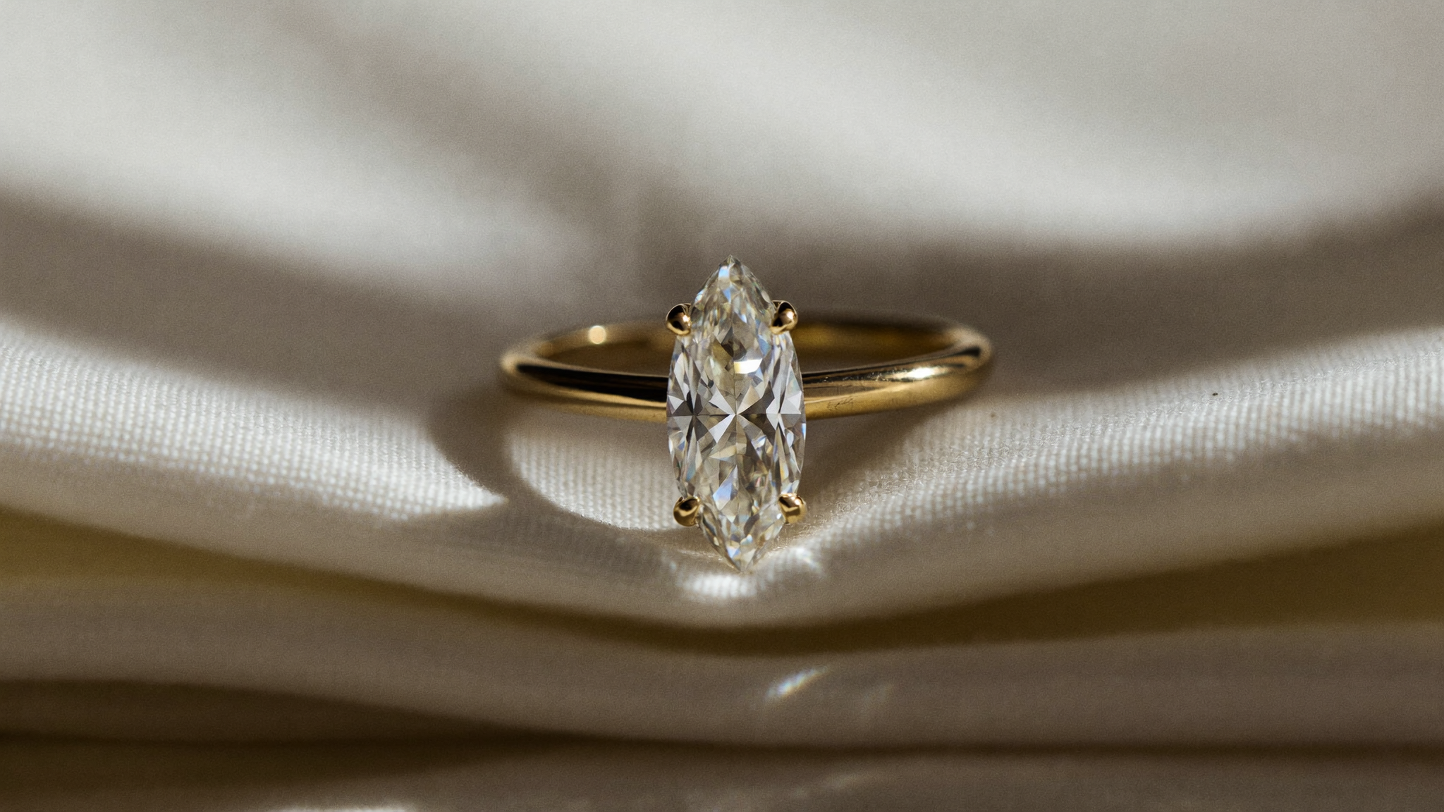 Marquise cut diamond solitaire ring in solid yellow gold resting on cream linen in soft natural light