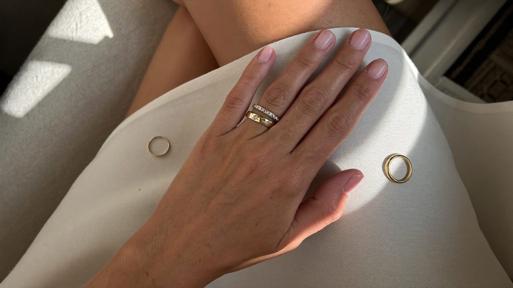 Stacked solid gold lab grown diamond bands on a hand beside two loose gold rings on linen, illustrating how to measure ring size at home