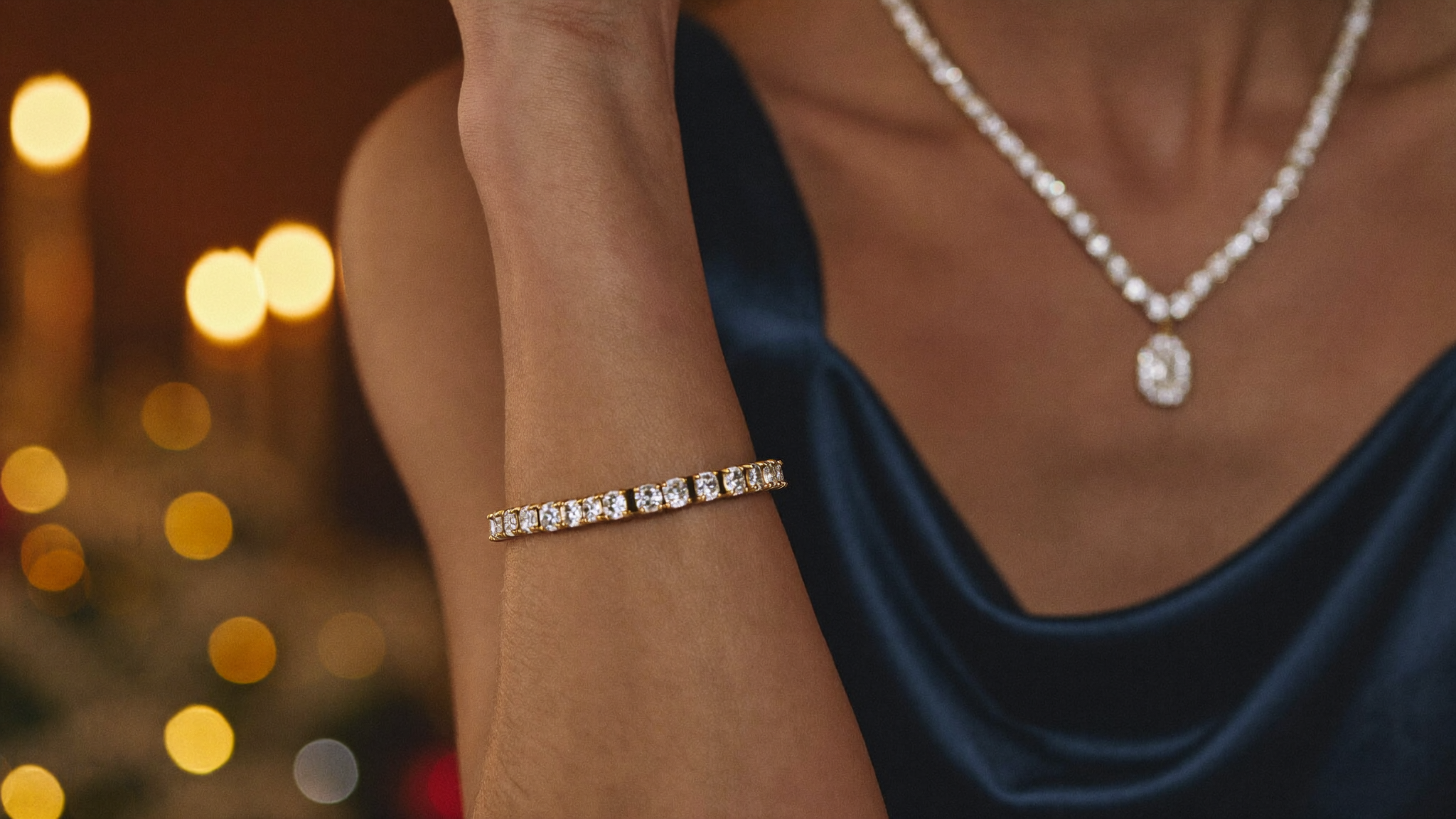 Holiday party jewelry: a gold diamond tennis bracelet and diamond pendant worn with a navy silk dress by candlelight