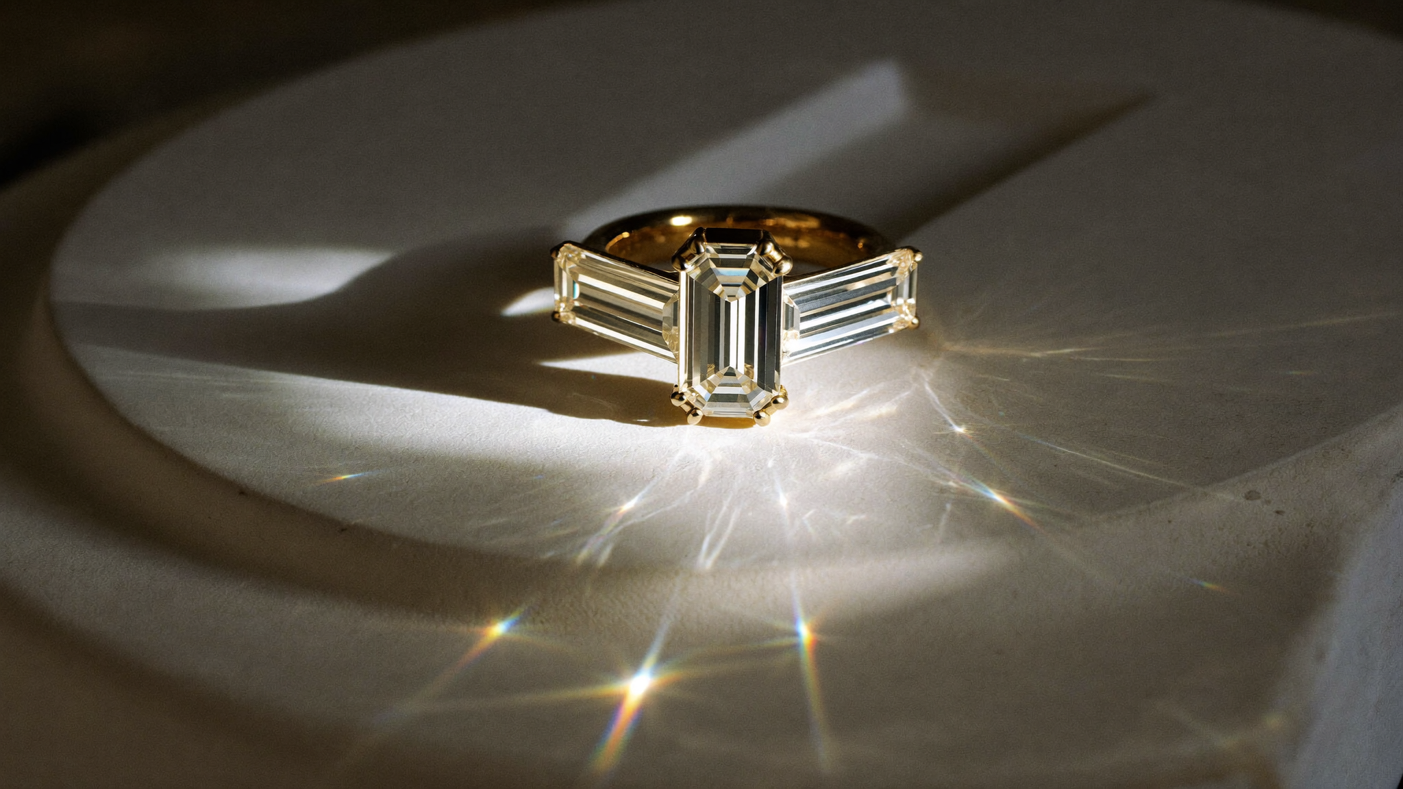 Emerald cut diamonds: a step-cut emerald diamond ring in yellow gold on cream stone in natural light